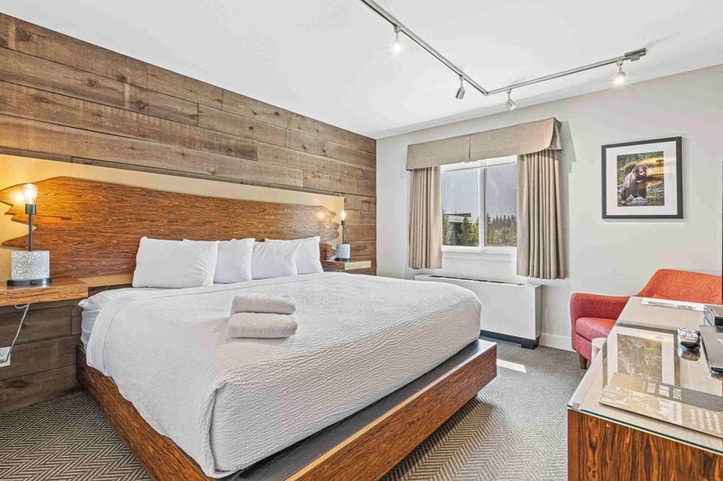 Helles Hotelzimmer mit King-Size-Bett, Holz-Kopfteil, Handtüchern und Fenster mit Waldblick.