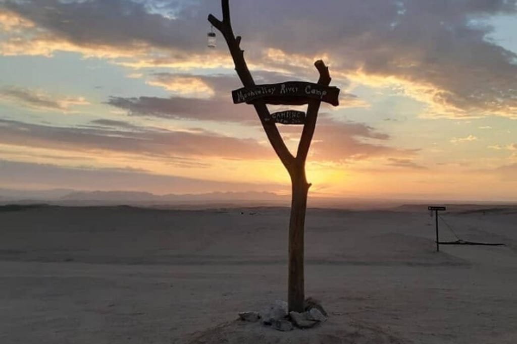 Holzschild-Silhouette in weiter Wüstenlandschaft bei Sonnenaufgang mit warmem Himmel