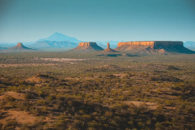 Weite Trockenlandschaft mit Dornbusch, mehreren Tafelbergen und warmem Licht am späten Nachmittag