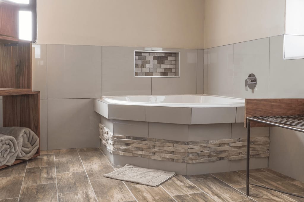Modernes Badezimmer mit eckiger Badewanne, Holzregal und Tageslicht, in neutralen Farben.