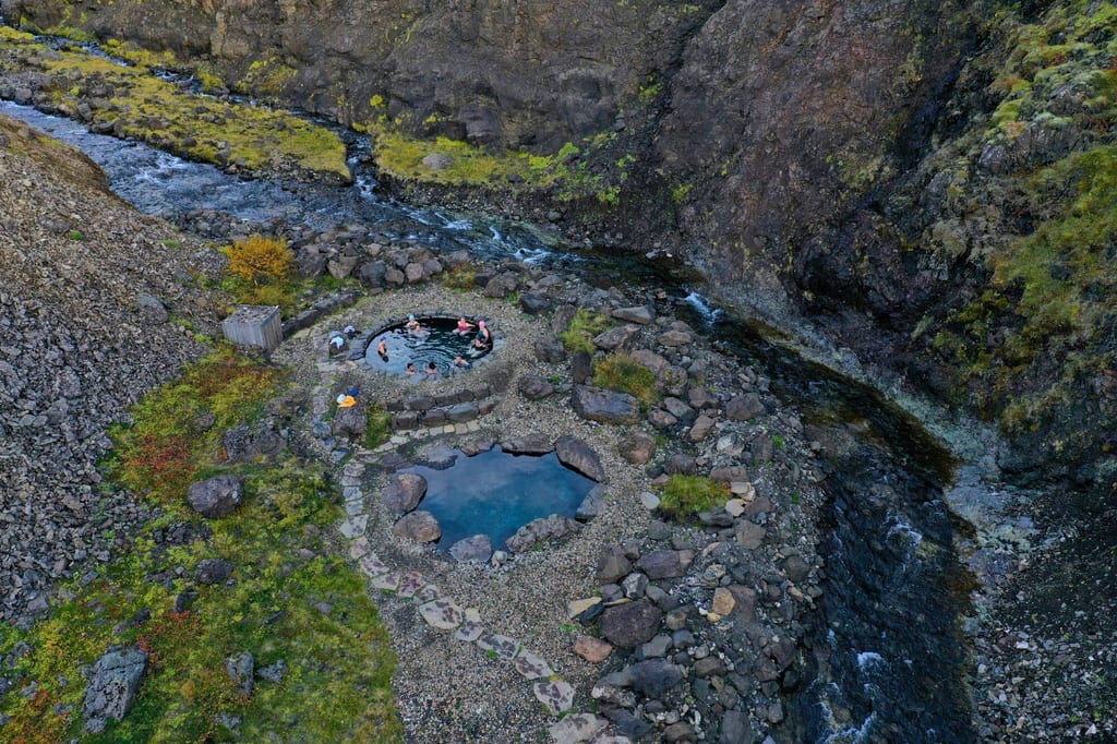 Luftbild zweier Thermalbecken an einem felsigen Bachufer mit Badenden und moosbewachsener Vegetation.