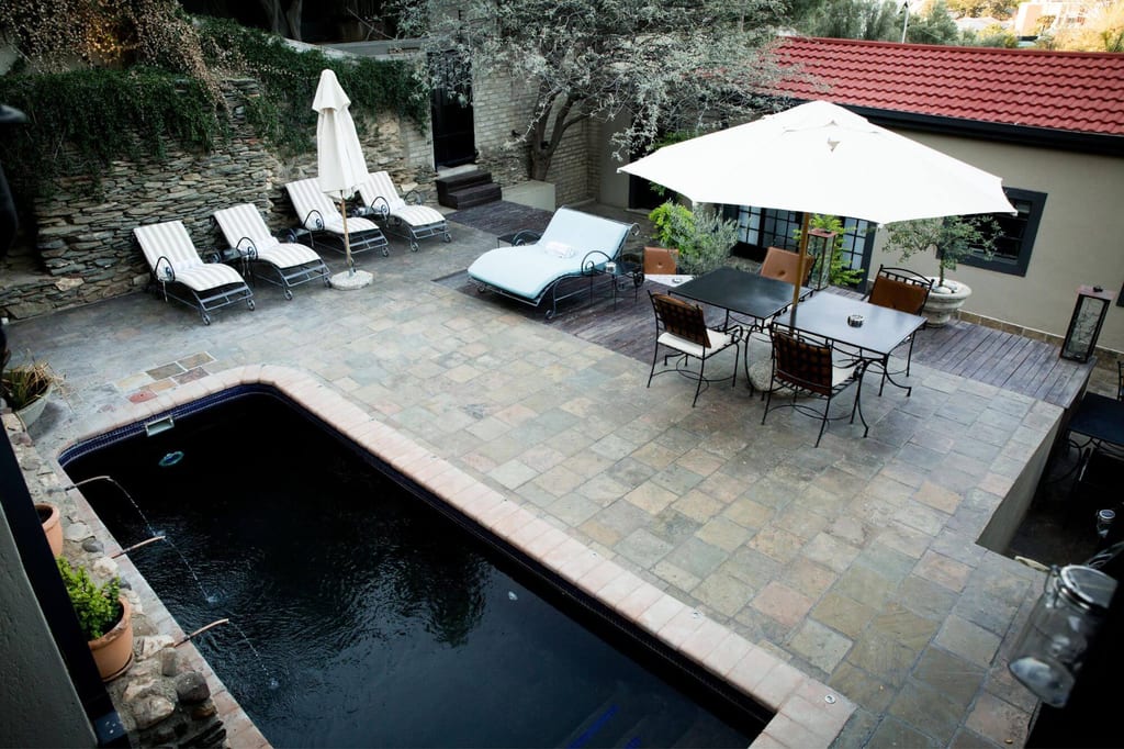 Blick von oben auf gepflasterte Terrasse mit Pool, Liegen und Sitzgruppe unter Sonnenschirm