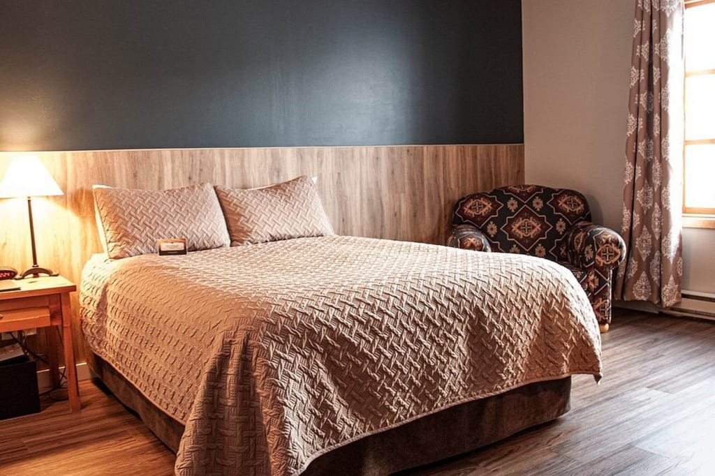 Gemütliches Schlafzimmer mit Doppelbett, Holzpaneel, Sessel und warmem Licht.