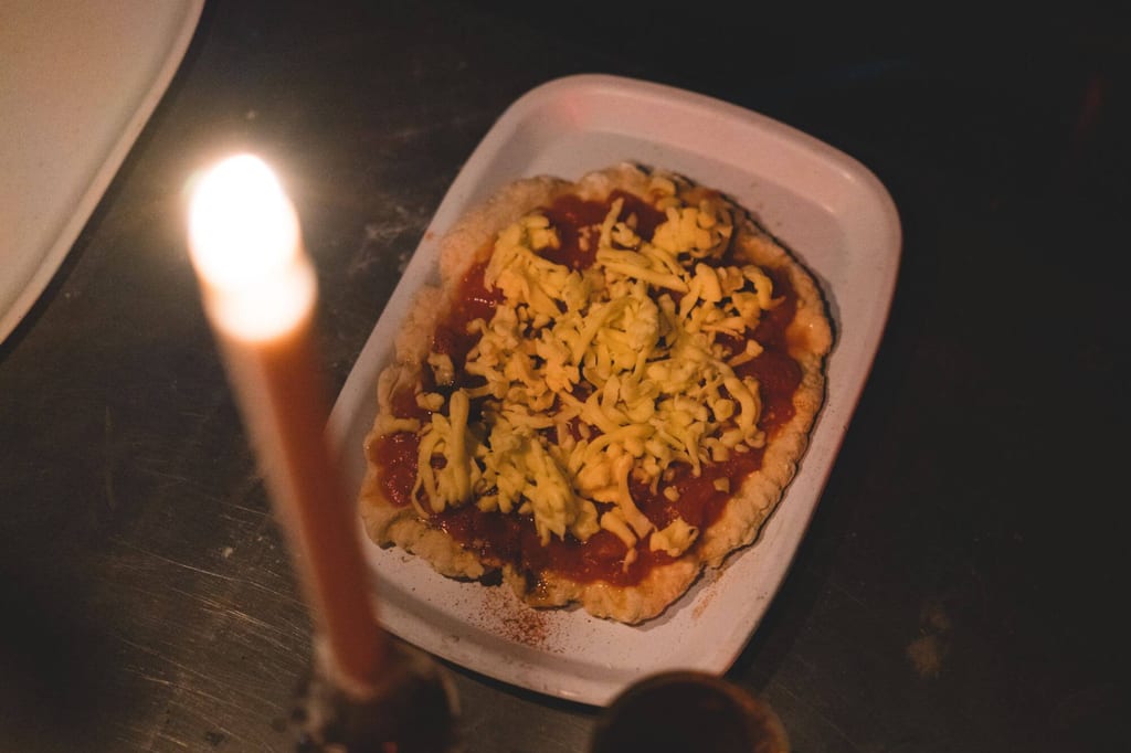 Belegtes Teiggebäck mit Tomatensauce und Käse auf weißem Teller bei Kerzenlicht