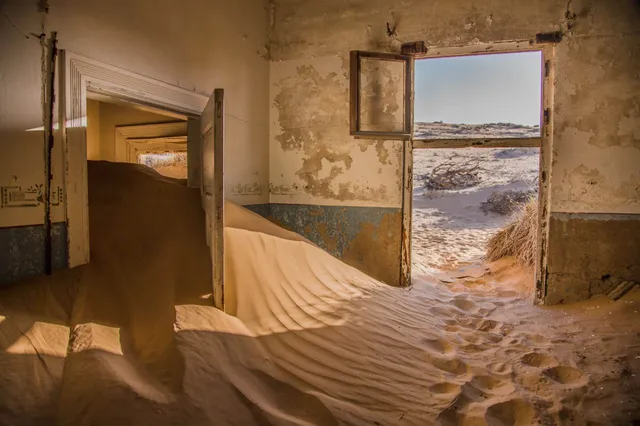 Verlassenes Haus, dessen Räume von Sanddünen gefüllt sind, mit offener Tür zum Außensand