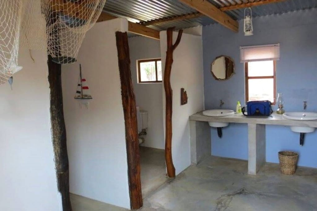 Rustikales Badezimmer mit zwei Waschbecken, Betonplatte, Holzbalken und Tageslichtfenstern.