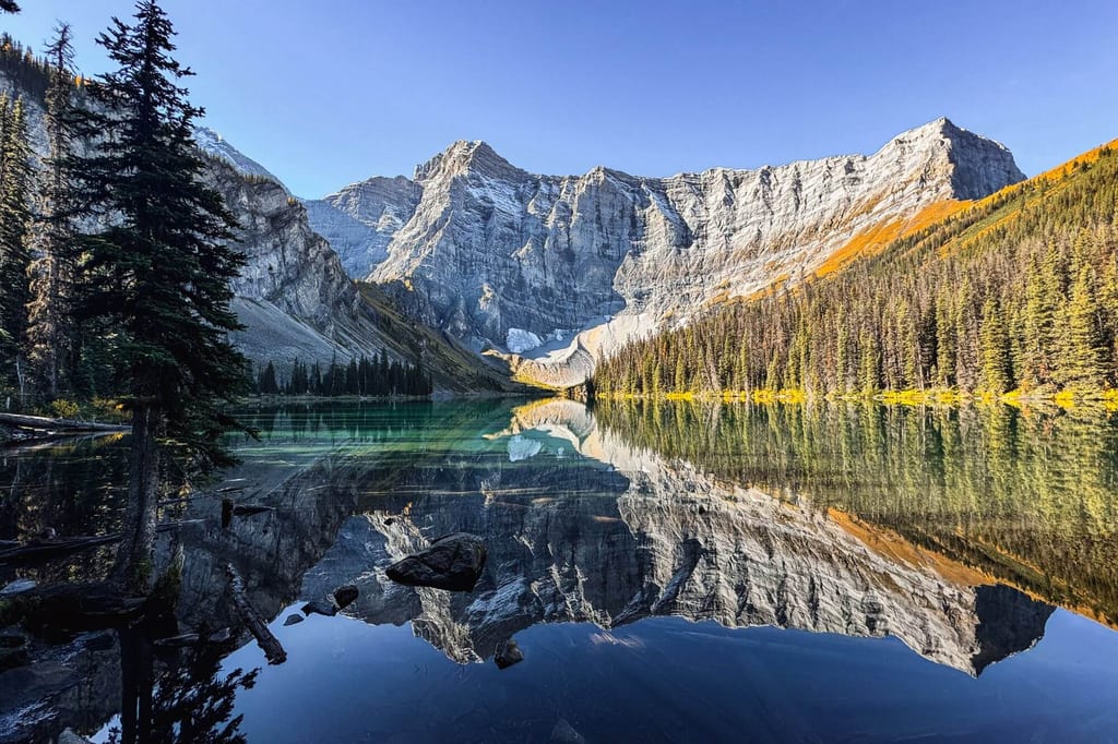 Bergsee mit spiegelglatter Reflexion der steilen Felswände und Nadelwälder, klarer Himmel