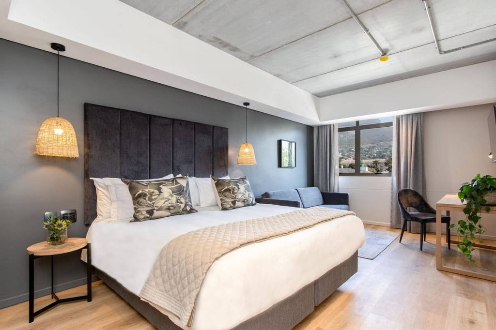 Modernes Hotelzimmer mit großem Doppelbett, Hängeleuchten, Sofa und Fenster mit Außenblick.