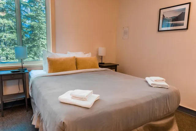 Aufgeräumtes Schlafzimmer mit Doppelbett, Handtüchern und Fenster mit Blick auf Bäume.