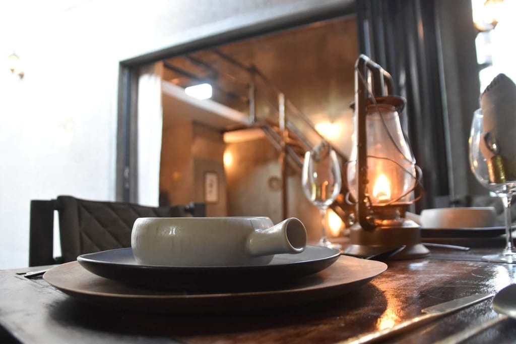 Gedeckter Holztisch mit Keramikschale, Tellern und brennender Petroleumlampe in warmer Abendstimmung.