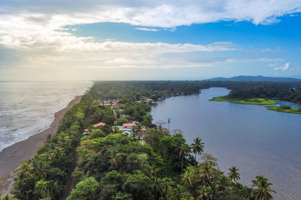 Luftaufnahme Küstenstreifen mit Palmen, Dorf und Flussmündung im Tortuguero Nationalpark, Costa Rica.