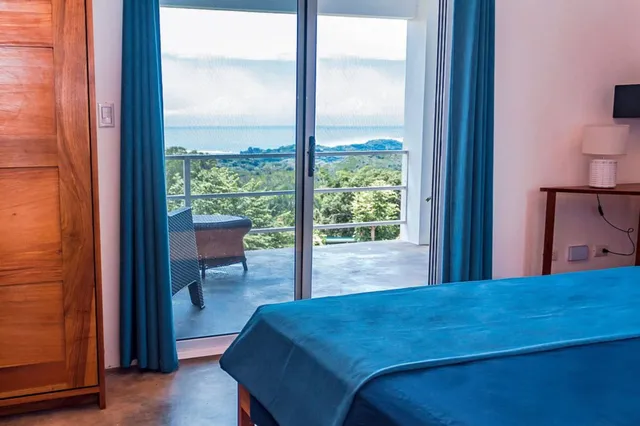 Schlafzimmer mit blauem Bett und offener Schiebetür zum Balkon mit Meerblick