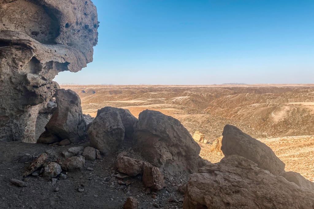 Blick aus einer Felsöffnung auf eine weite, sandfarbene Hügellandschaft unter klarem blauem Himmel.
