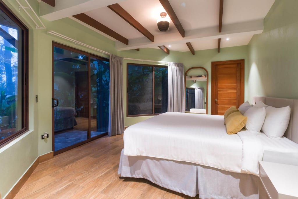 Gemütliches Schlafzimmer mit großem Bett, Holzboden und großen Glas-Schiebetüren zum Außenbereich.