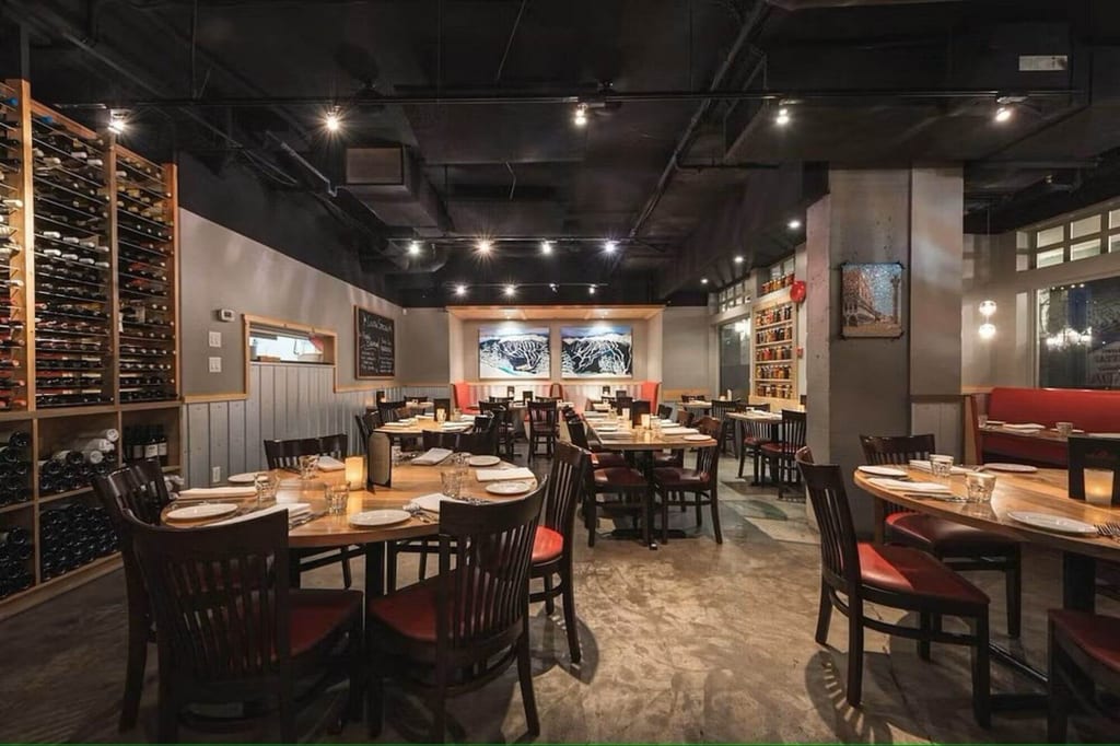 Innenraum eines stilvollen, warm beleuchteten Restaurants mit gedeckten Tischen und Weinregal.