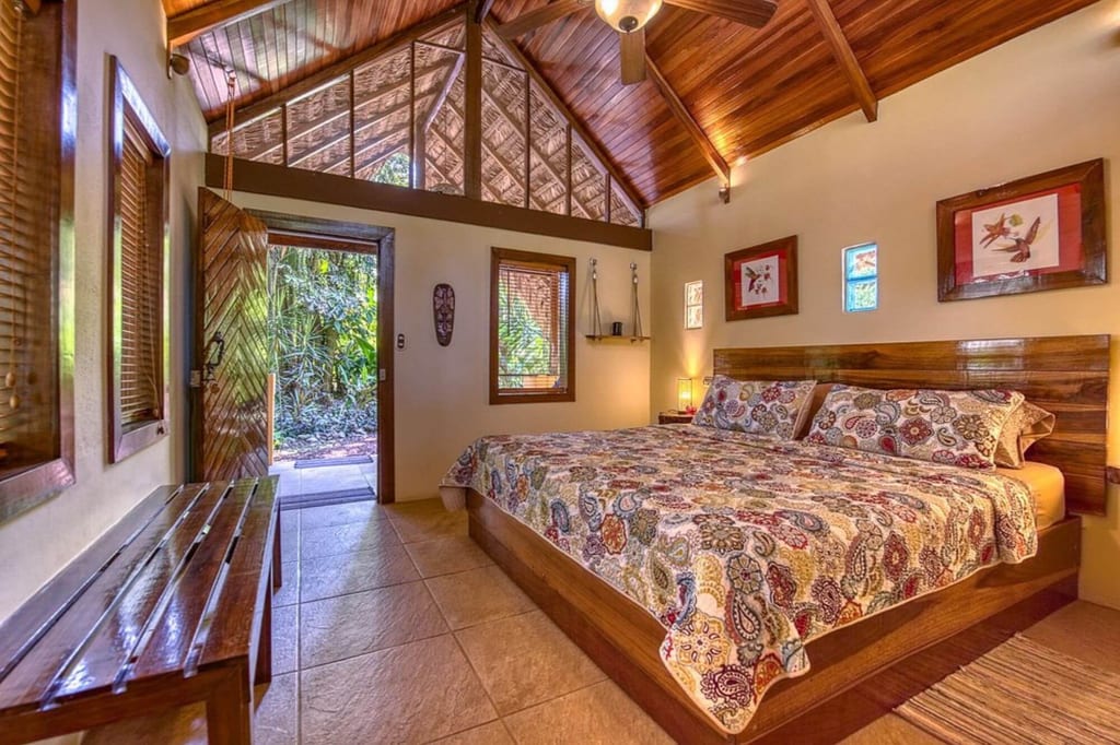Gemütliches Schlafzimmer mit großem Bett, Holzdecke und offener Tür zum grünen Außenbereich.