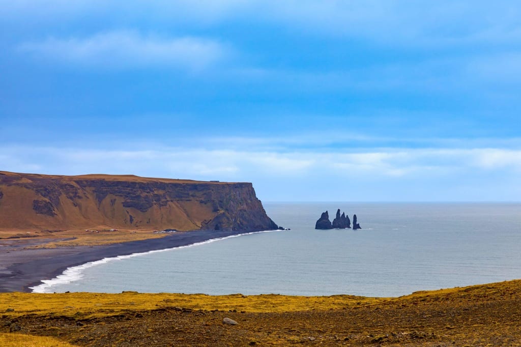 Küstenpanorama mit Klippen, schwarzem Strand und felsigen Seenädeln bei bewölktem Licht, Blick von oben