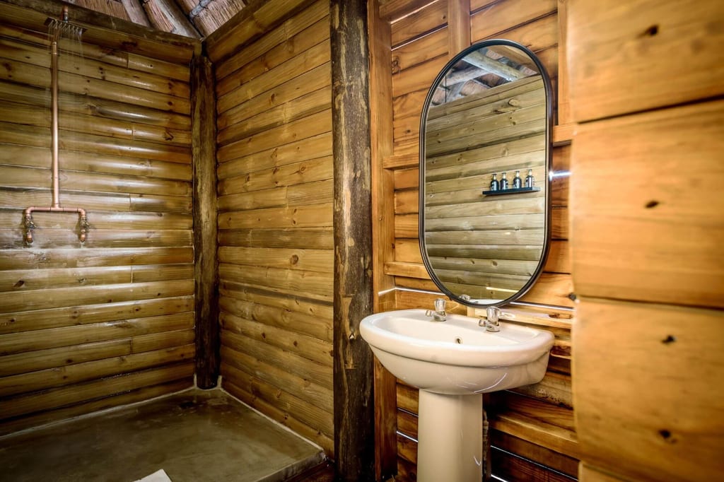 Rustikales Badezimmer mit weißem Waschbecken, ovalem Spiegel und offener Dusche in Holzverkleidung