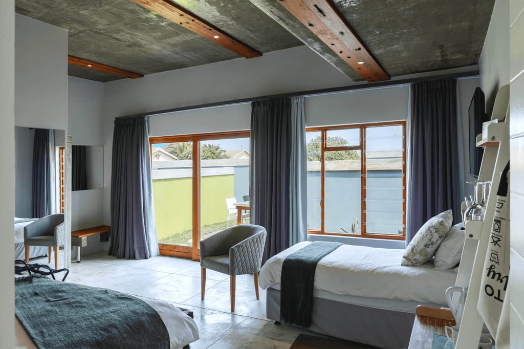 Helles modernes Doppelzimmer mit zwei Einzelbetten, großen Fenstern und sichtbarer Betondecke.