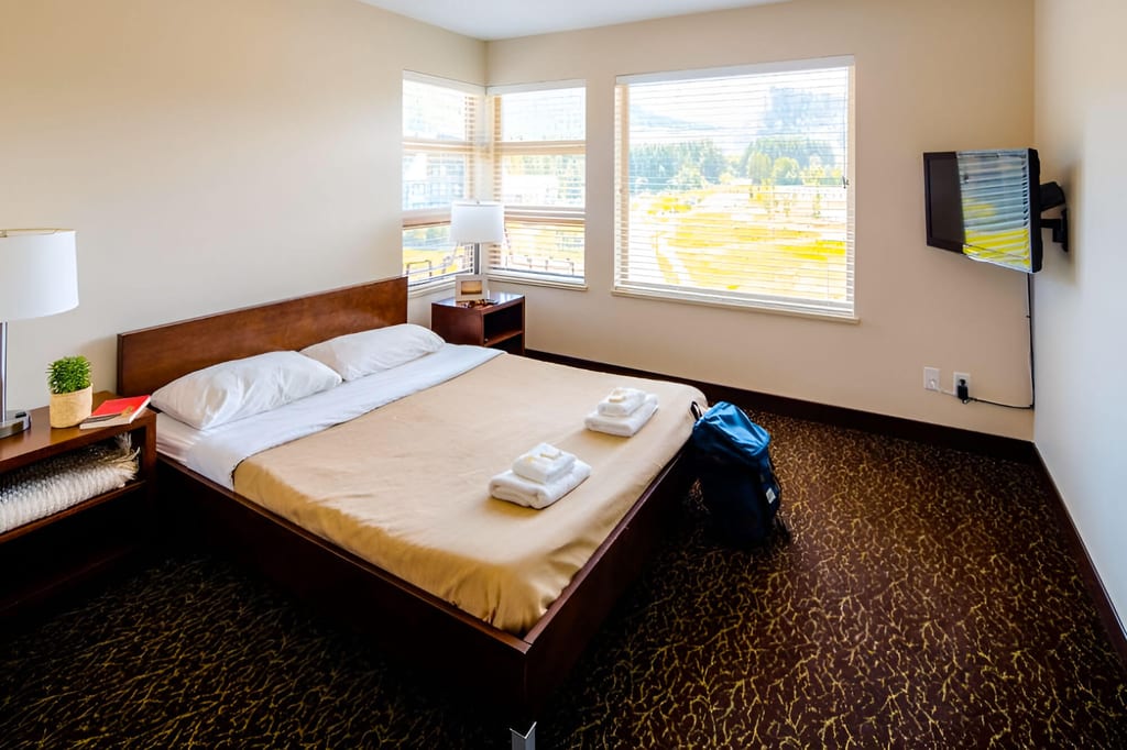 Helles, aufgeräumtes Hotelzimmer mit Doppelbett, Handtüchern und Rucksack bei Tageslicht