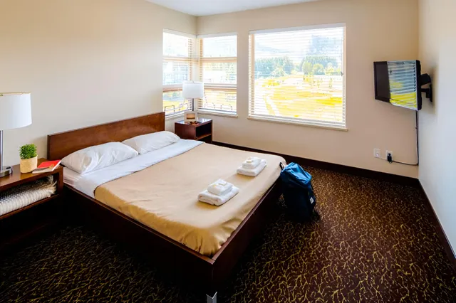 Helles, aufgeräumtes Hotelzimmer mit Doppelbett, Handtüchern und Rucksack bei Tageslicht