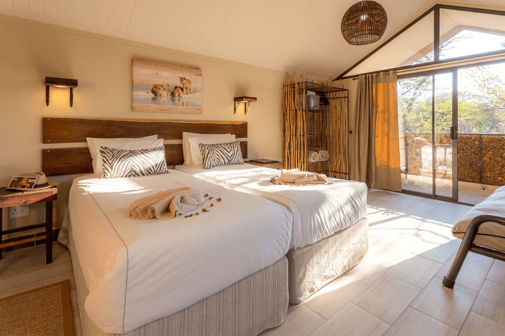 Helles Doppelzimmer mit zwei Einzelbetten, Zebra‑Kissen und Balkon im warmen Nachmittagslicht.