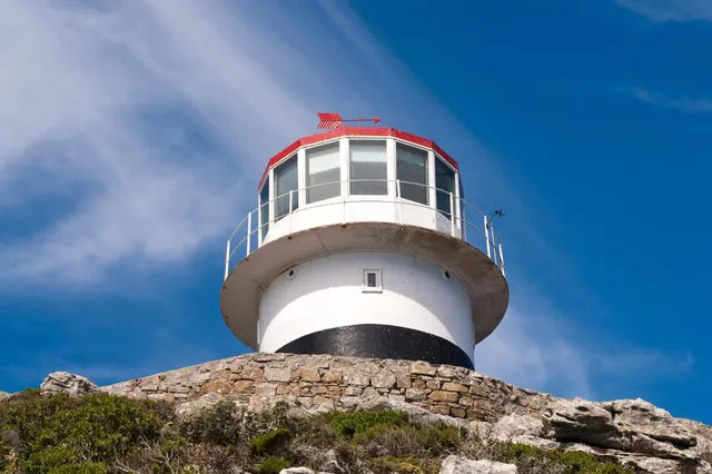 Weißer Leuchtturm auf felsigem Hügel vor tiefblauem Himmel, seitliche Untersicht