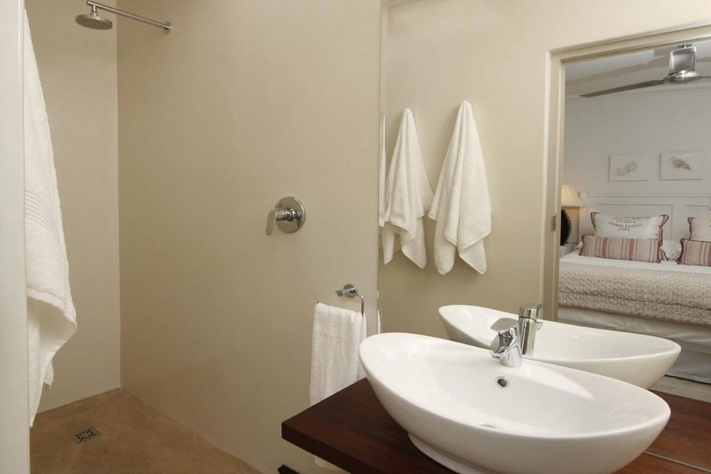 Helles Badezimmer mit zwei Aufsatzwaschbecken, Handtüchern und Spiegel, in dem ein Schlafzimmer reflektiert ist.