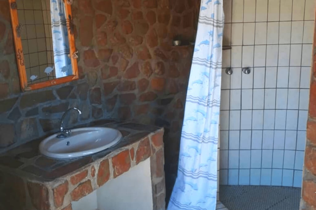 Rustikales Badezimmer mit steinverkleidetem Waschbecken und gefliester Dusche mit Duschvorhang.