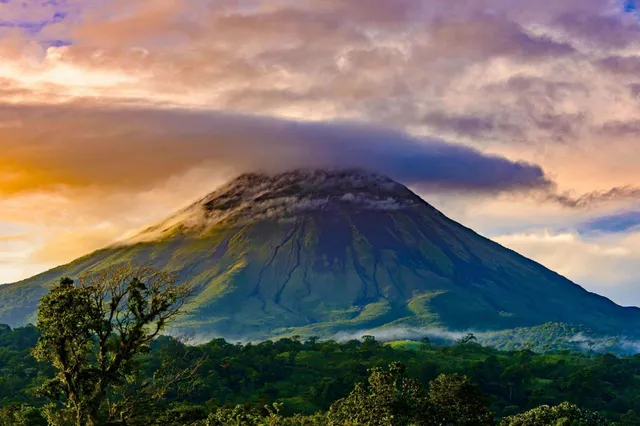 Vulkan mit Wolkenhut über grüner Regenwaldlandschaft in Costa Rica bei warmem Licht