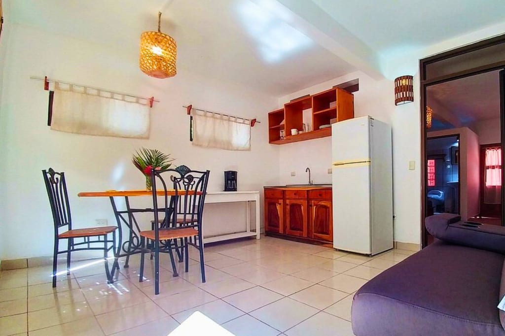 Helle Wohnküche mit Esstisch, Holzschränken und weißem Kühlschrank, Blick in angrenzendes Zimmer.