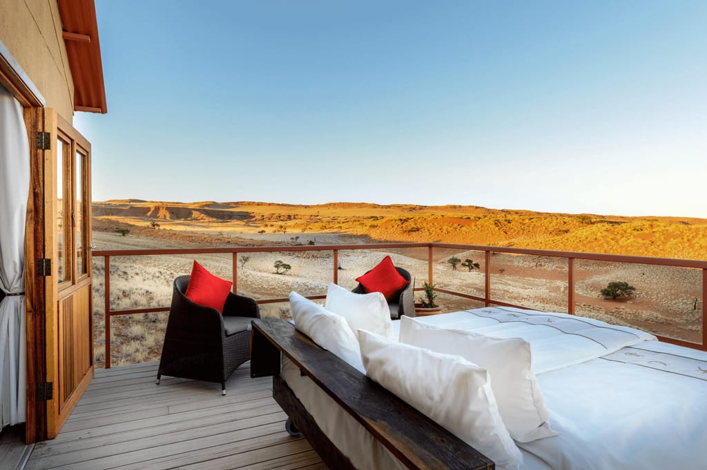 Lodge-Terrasse mit offenem Bett und Sesseln blickt auf goldene, weite Wüstenhügel