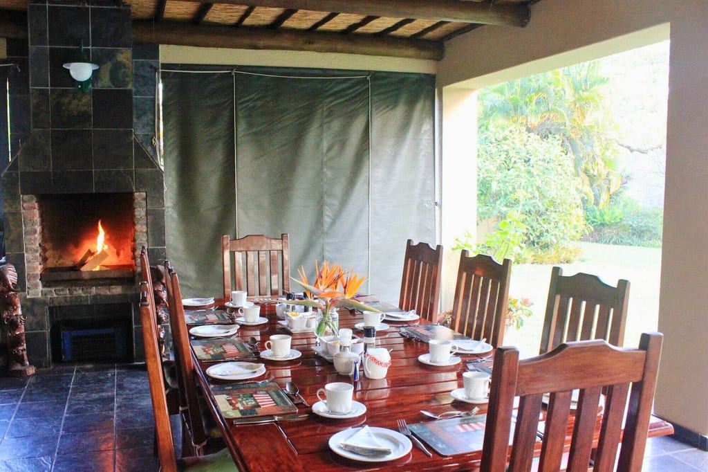 Gedeckter Holztisch in überdachtem Essbereich mit brennendem Kamin und Gartenblick