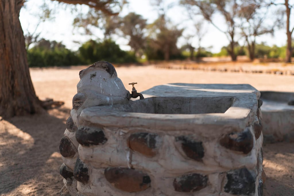 Nahaufnahme eines steinernen Außenspülbeckens mit Metall-Wasserhahn in sonniger, trockener Landschaft