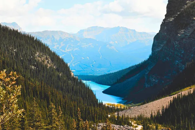 Talblick auf türkisen Gebirgssee zwischen Nadelwäldern und steilen Felswänden bei Tageslicht