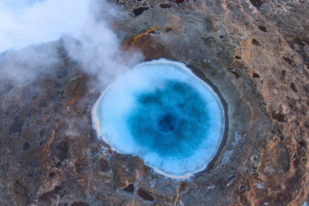 Luftaufnahme eines kreisrunden, tiefblauen Thermalbeckens mit aufsteigendem Dampf