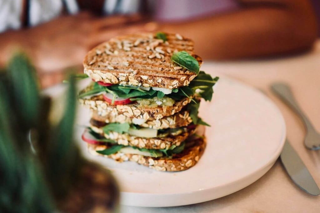 Mehrlagiges Vollkorn-Sandwich mit grünem Salat und Gemüse auf weißem Teller, Nahaufnahme