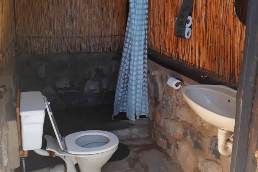 Rustikale Außentoilette mit WC, Waschbecken, Duschvorhang und Schilfwand