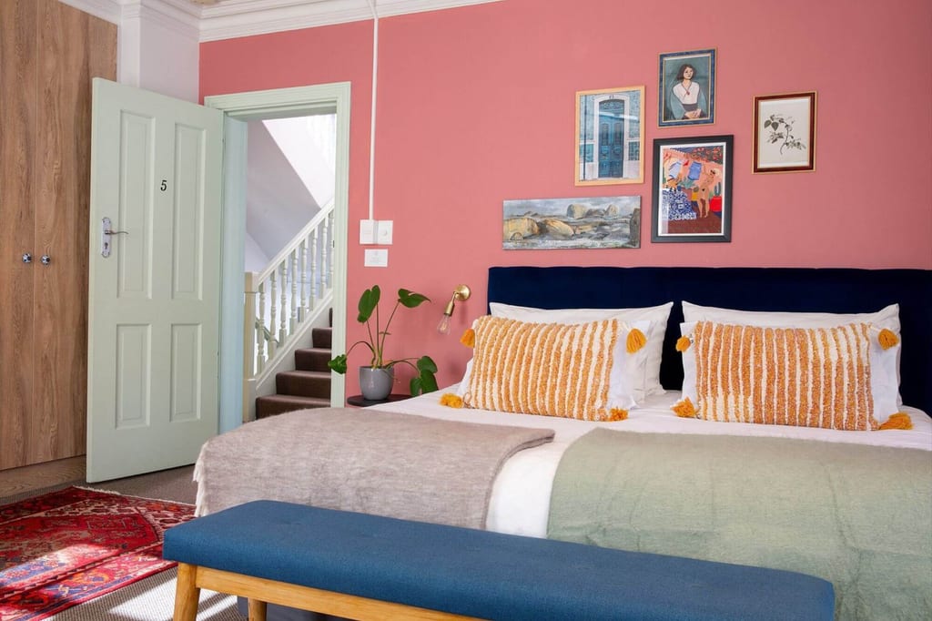 Gemütliches Doppelzimmer mit rosa Wand, großem Bett und offener Tür zum Treppenhaus