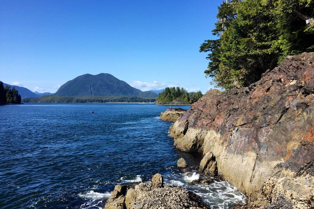 Felsige Küste mit blauem Meer, bewaldeter Insel und Berg bei klarem sonnigem Himmel