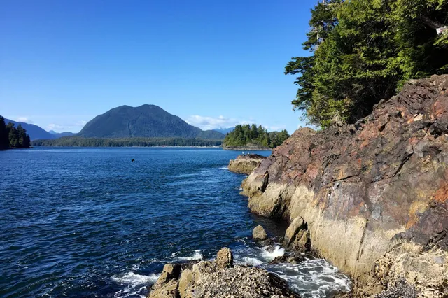 Felsige Küste mit blauem Meer, bewaldeter Insel und Berg bei klarem sonnigem Himmel
