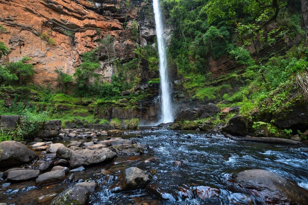 Hoher Wasserfall stürzt in einen steinigen Bach vor bewachsener Felswand