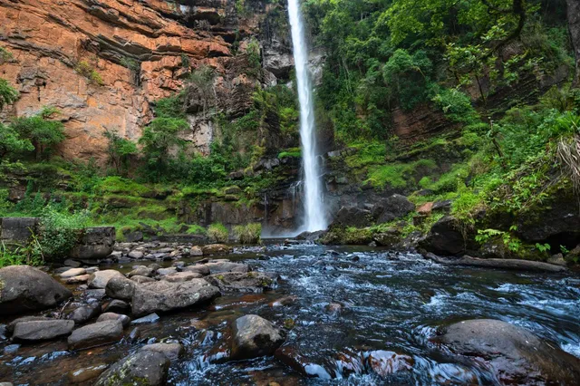 Hoher Wasserfall stürzt in einen steinigen Bach vor bewachsener Felswand