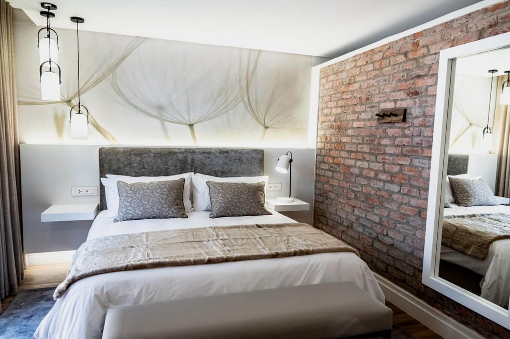 Modernes Schlafzimmer mit Doppelbett, Sichtbacksteinwand und großem Wandspiegel, warmes Licht.