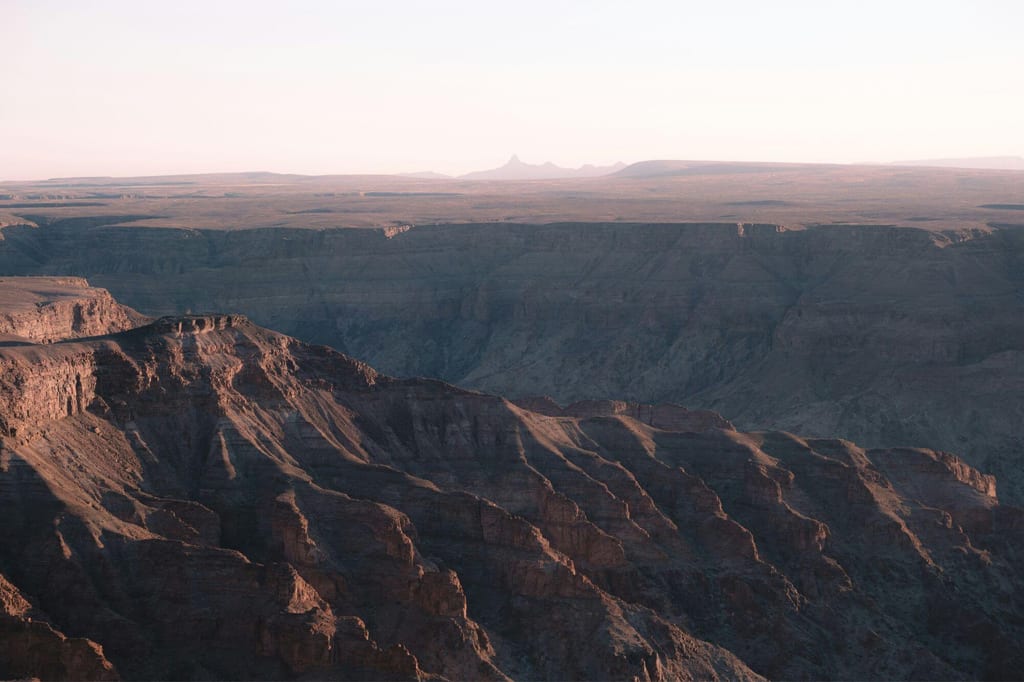Panoramablick auf den Fish River Canyon in Namibia mit pastellfarbenem Himmel und warm betonten Felsklippen.