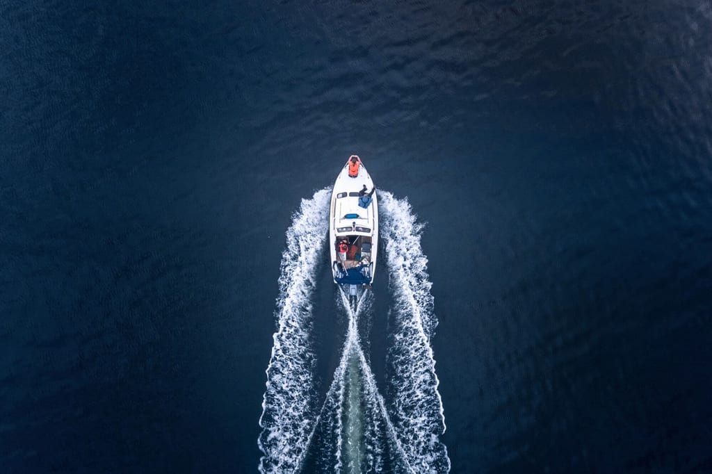 Vogelperspektive auf ein Motorboot, das eine Gischtspur über dunkles Wasser zieht.