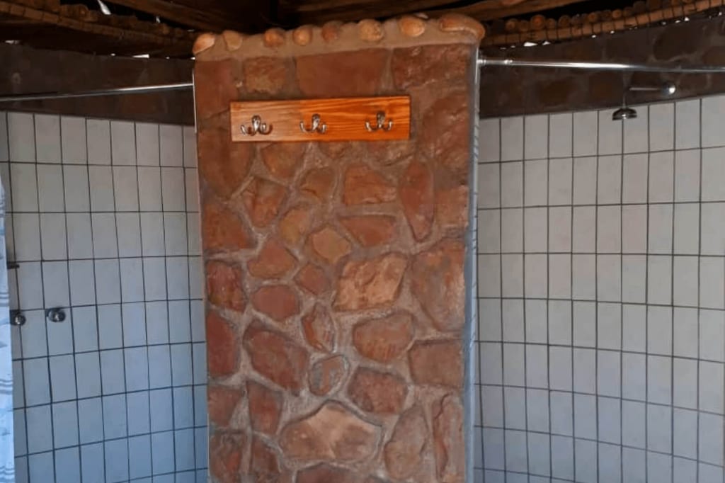 Frontale Ansicht einer Duschanlage mit Steinsäule, Holzhaken und gefliesten Wänden