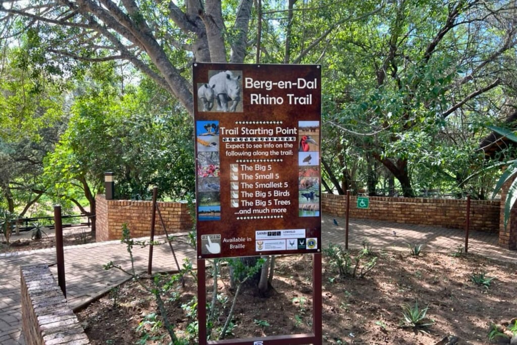 Informationstafel ‚Berg-en-Dal Rhino Trail‘ am Wegesrand in schattiger Parklandschaft bei Tageslicht