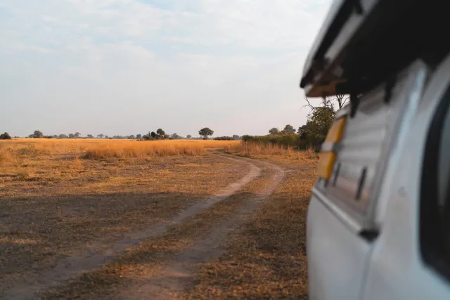 Geschwungene Sandpiste durch trockenes Grasland mit Safari-Fahrzeug im Vordergrund, Nkasa Rupara, Namibia