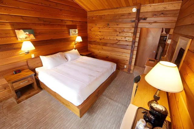 Gemütliches Hotelzimmer mit Holzwänden, Doppelbett, Schreibtisch und warmer Beleuchtung